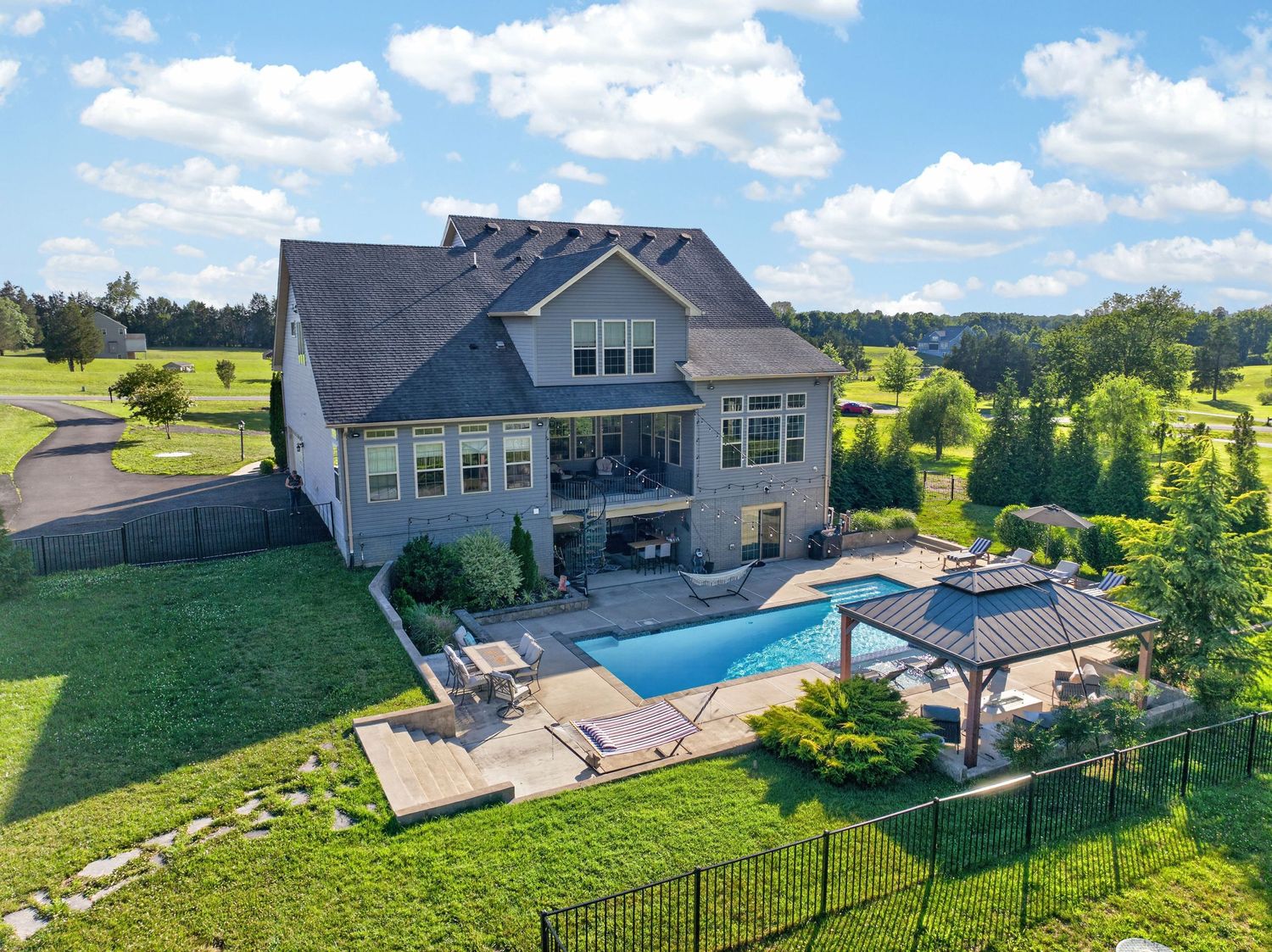 Aerial view of a large two-story home with a backyard pool, gazebo, and lush green lawn on a sunny day.