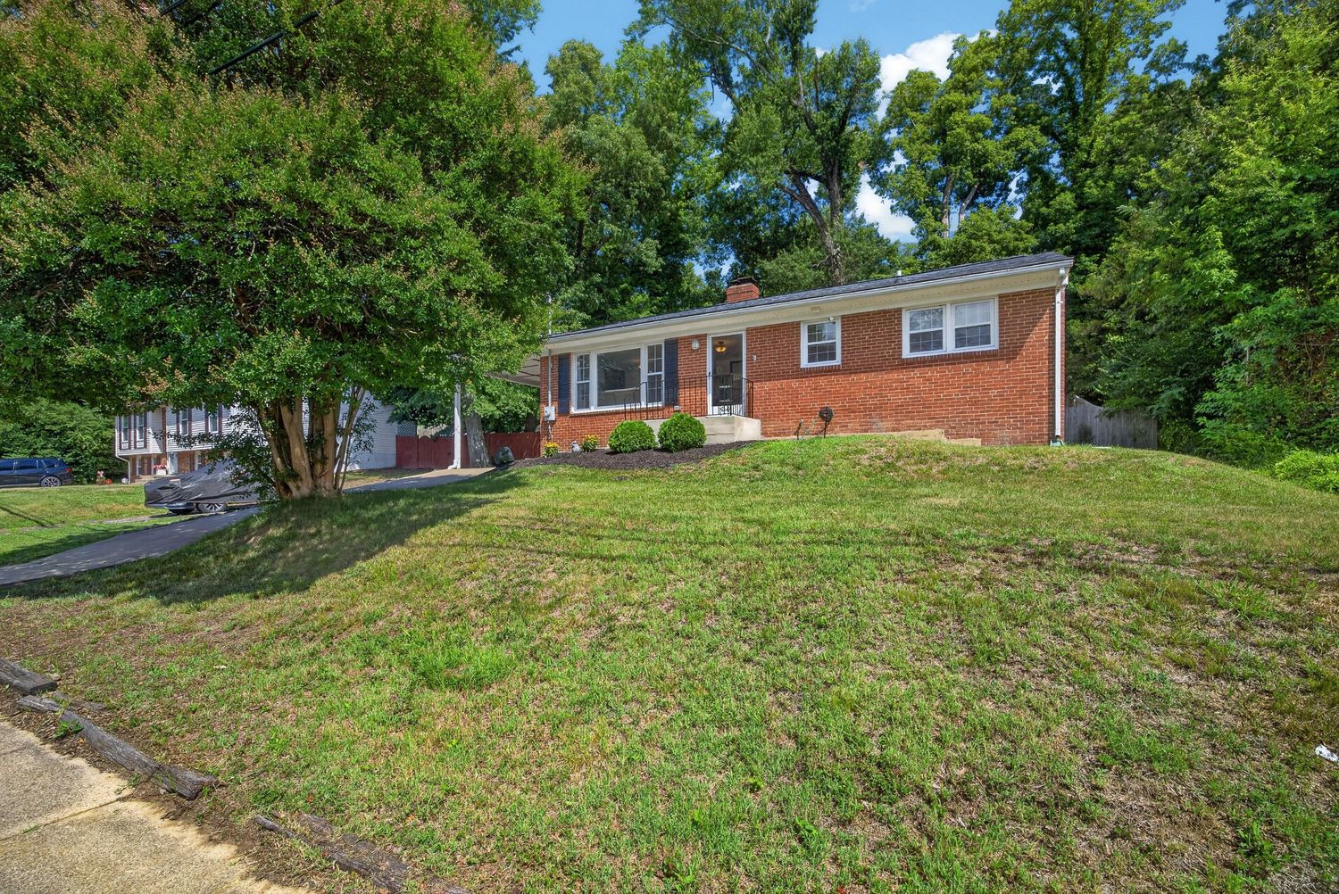 Brick ranch-style home with lush green lawn, mature trees, and classic red brick exterior on a gentle hill.