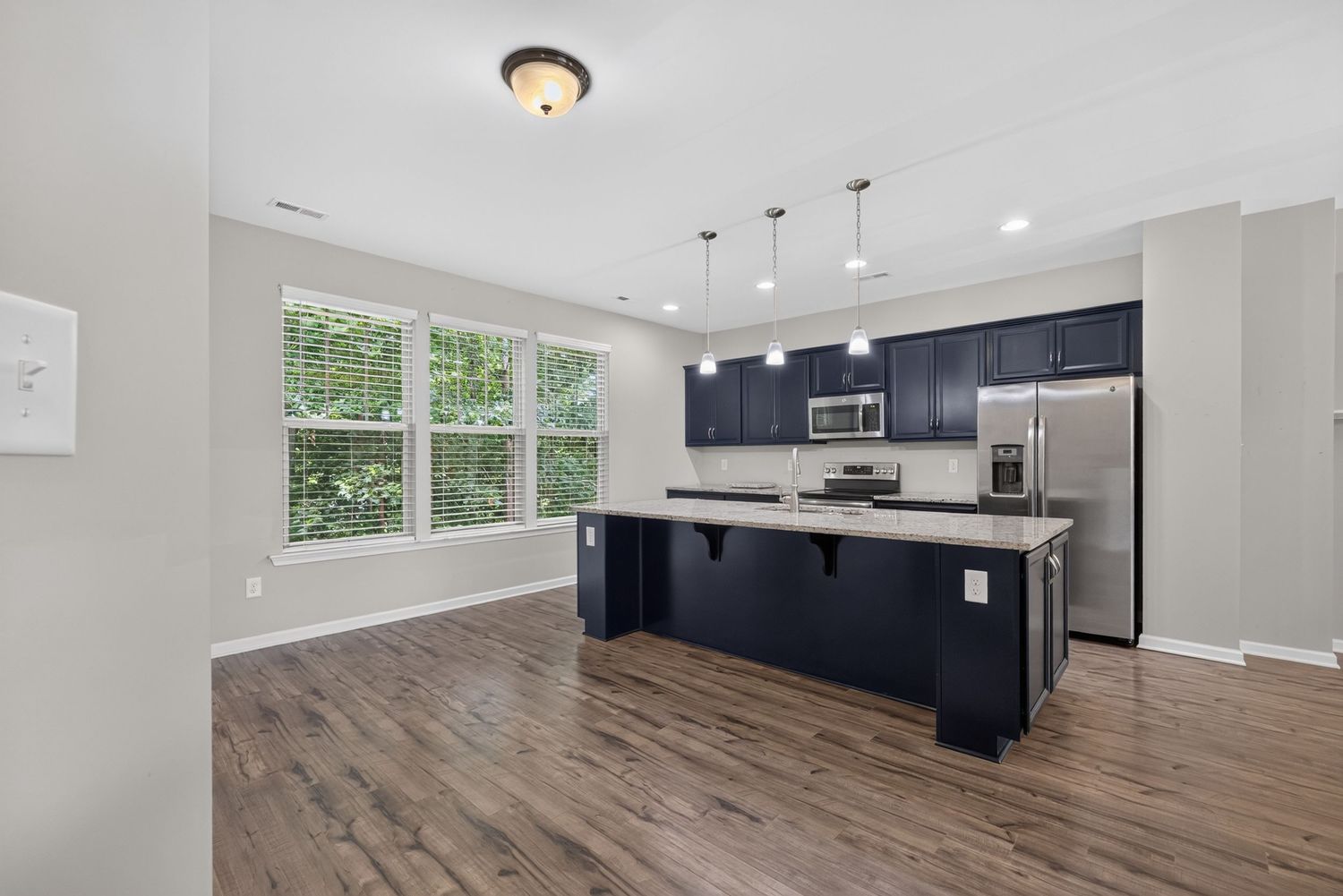 Modern kitchen with dark navy cabinets, stainless steel appliances, island with pendant lights, and hardwood floors.