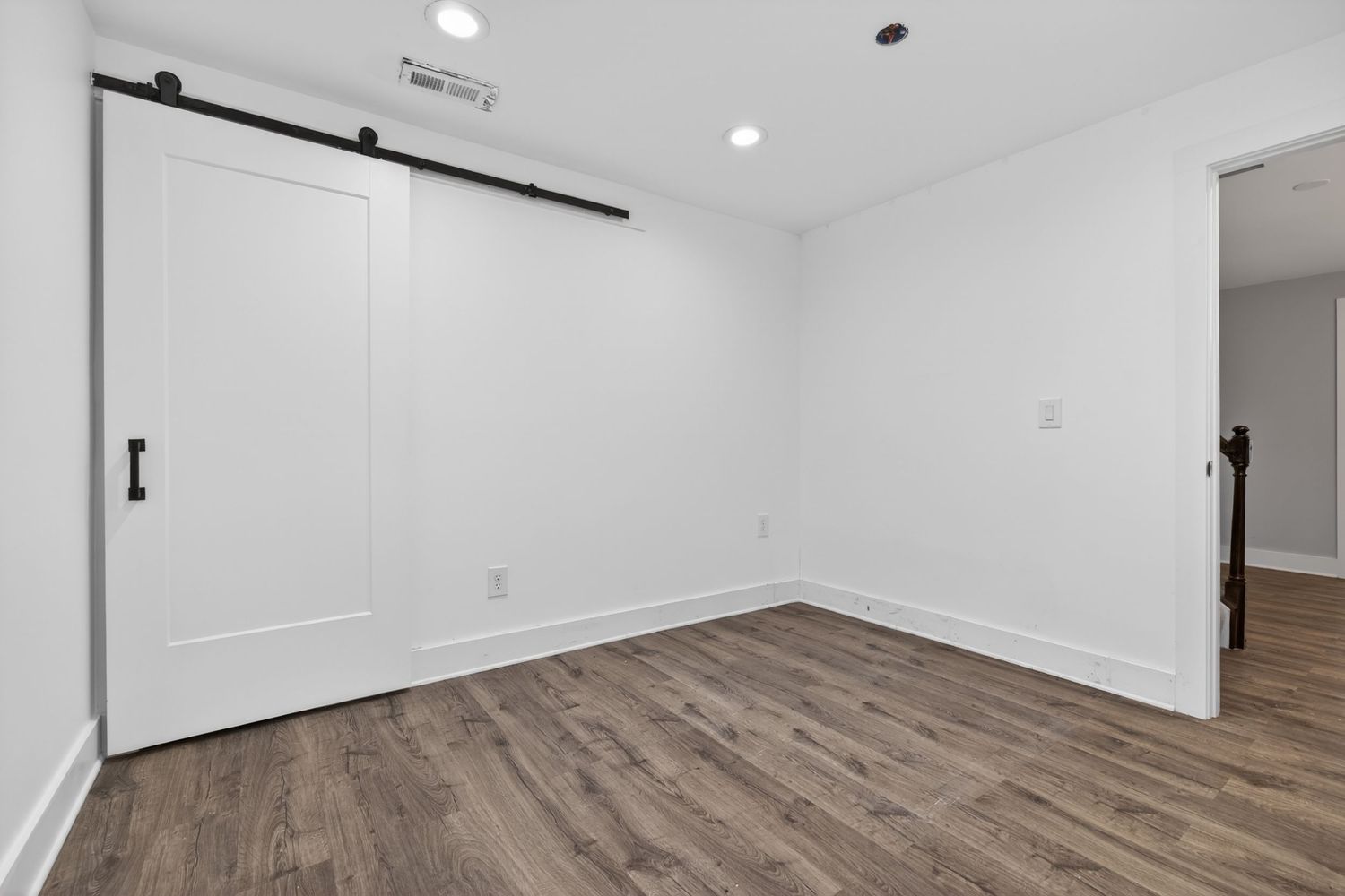 Bright empty room with white barn sliding door, recessed lighting, and medium-toned hardwood floors in a modern home.