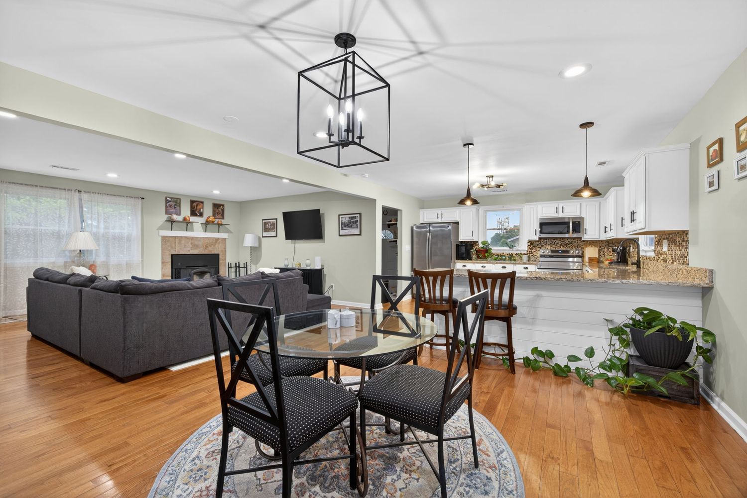 Open-concept dining area with hardwood floors, black chandelier, and modern kitchen with white cabinets in background.