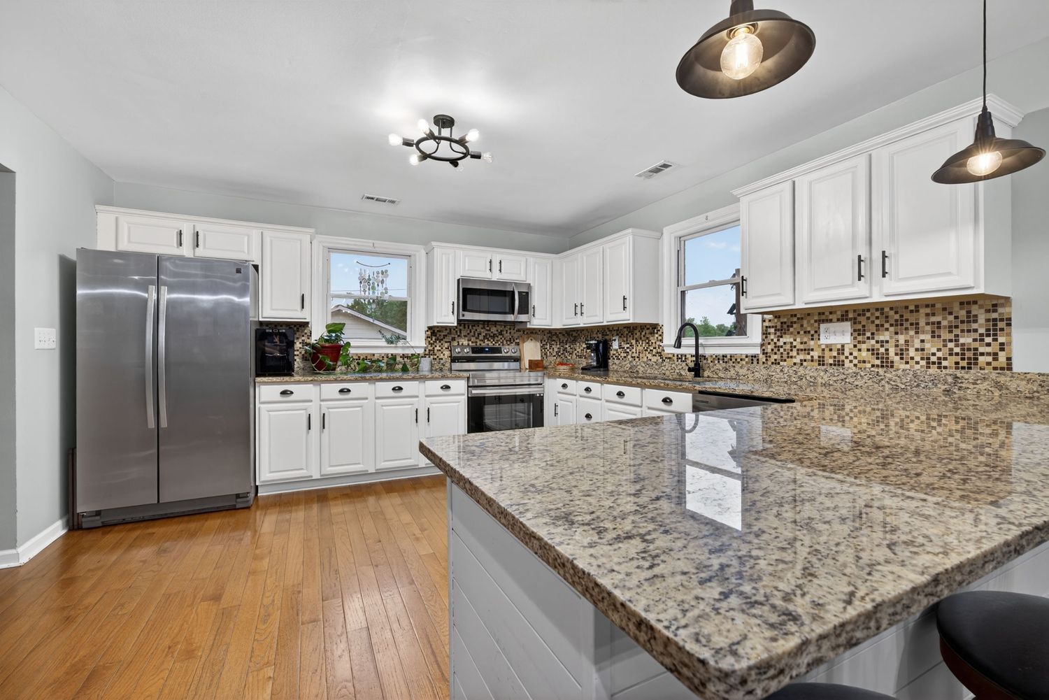 Modern kitchen with white cabinets, granite countertops, stainless steel appliances, mosaic backsplash, and hardwood floors.