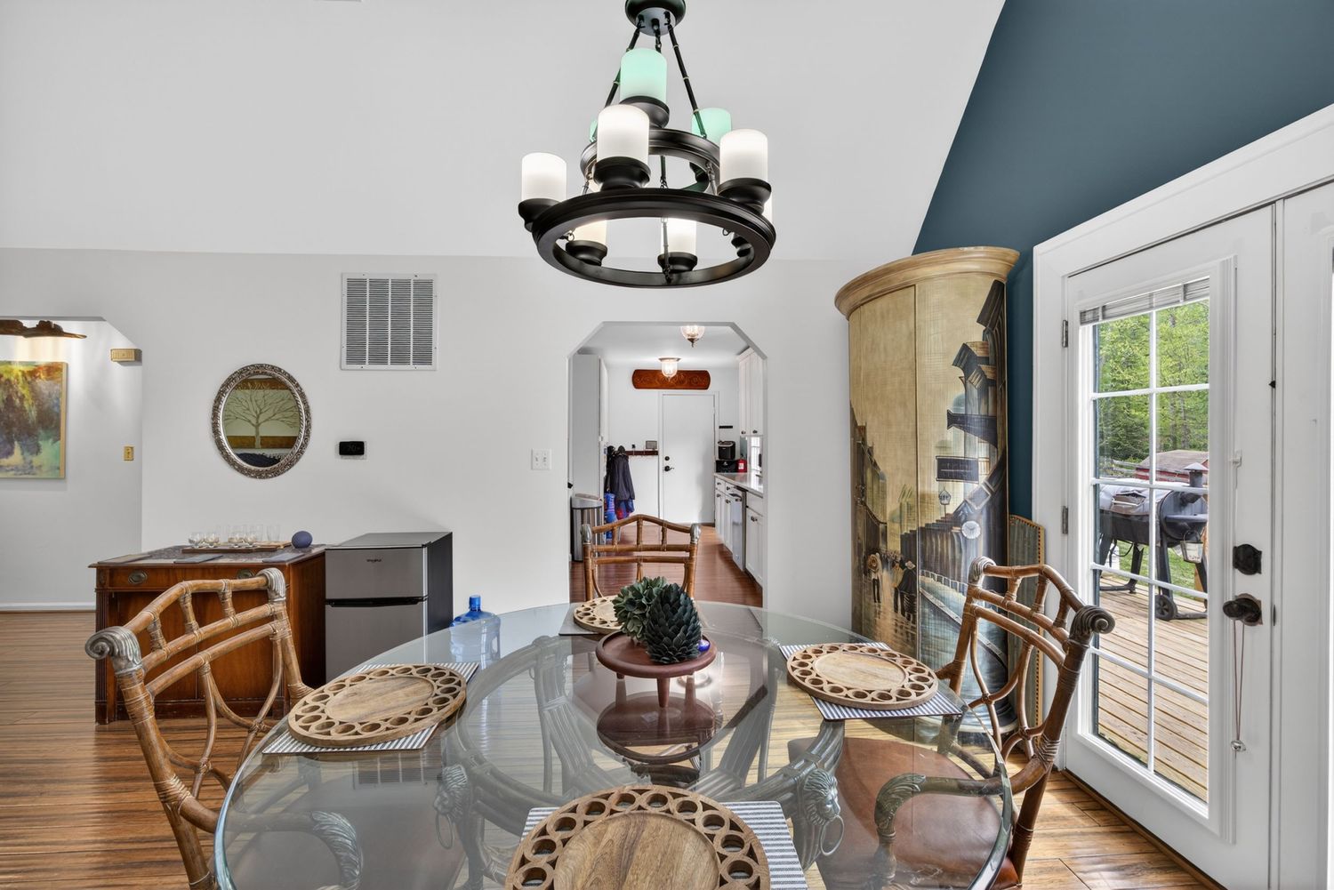 Dining room with glass table, wicker chairs, chandelier, hardwood floors, arched doorway, and French doors with natural light.