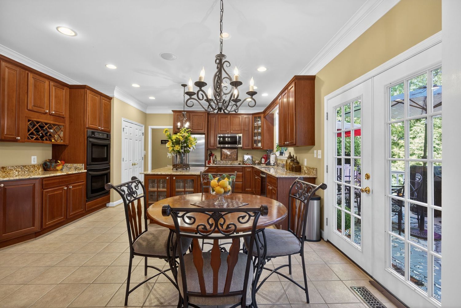 Elegant kitchen with cherry wood cabinets, chandelier, round dining table, and French doors leading to a lush garden.