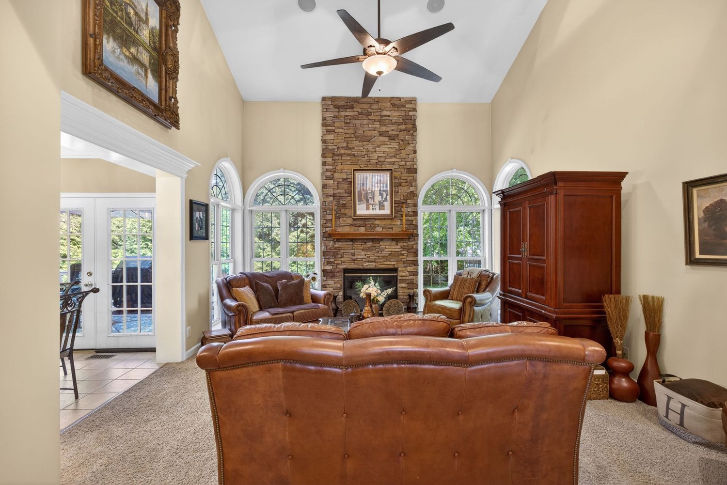 Elegant living room with vaulted ceiling, stone fireplace, arched windows, leather sofa, and ceiling fan.