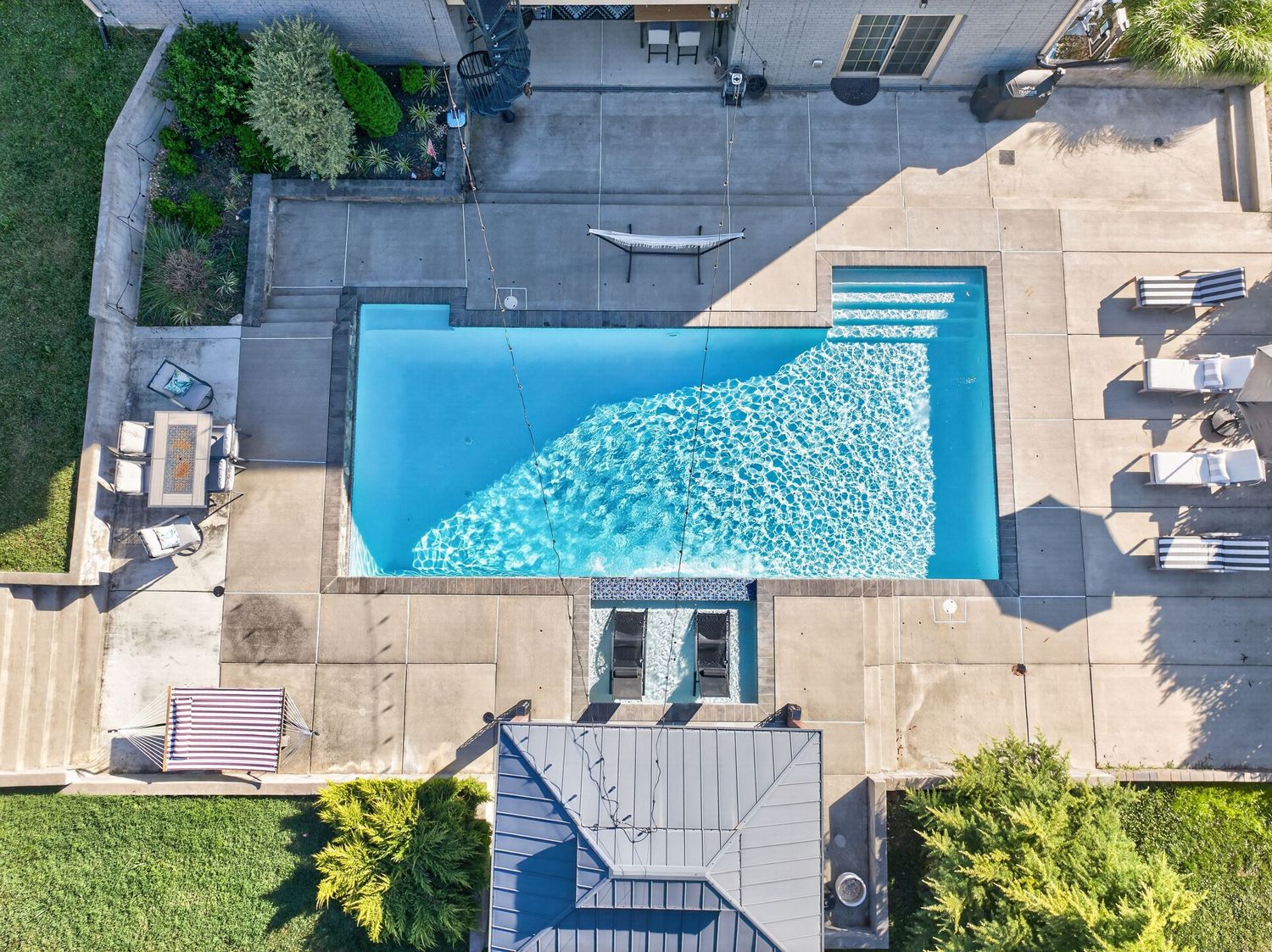 Aerial view of a rectangular backyard swimming pool with blue water, surrounded by a spacious patio and lounge chairs.