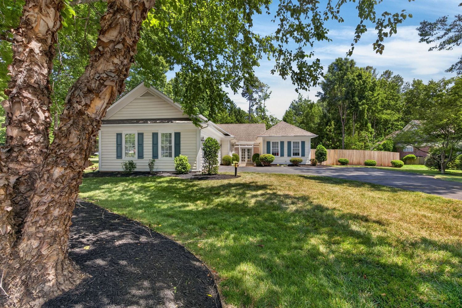 Charming single-story home with lush green lawn, mature trees, and a welcoming facade on a sunny day.