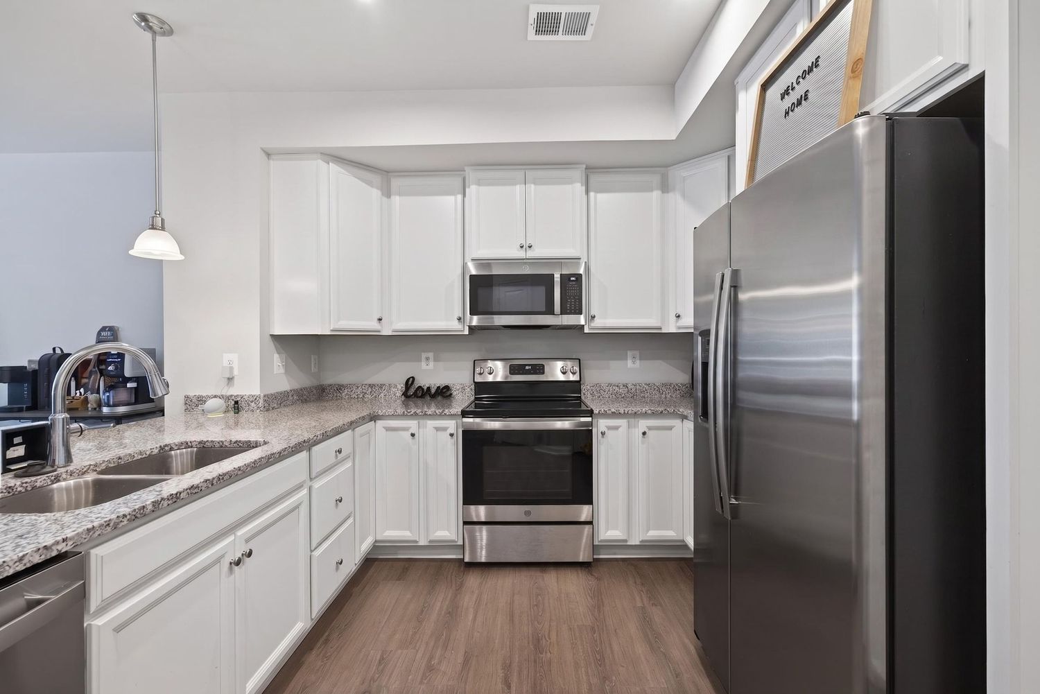Modern kitchen with white cabinets, granite countertops, stainless steel appliances, and dark hardwood floors.