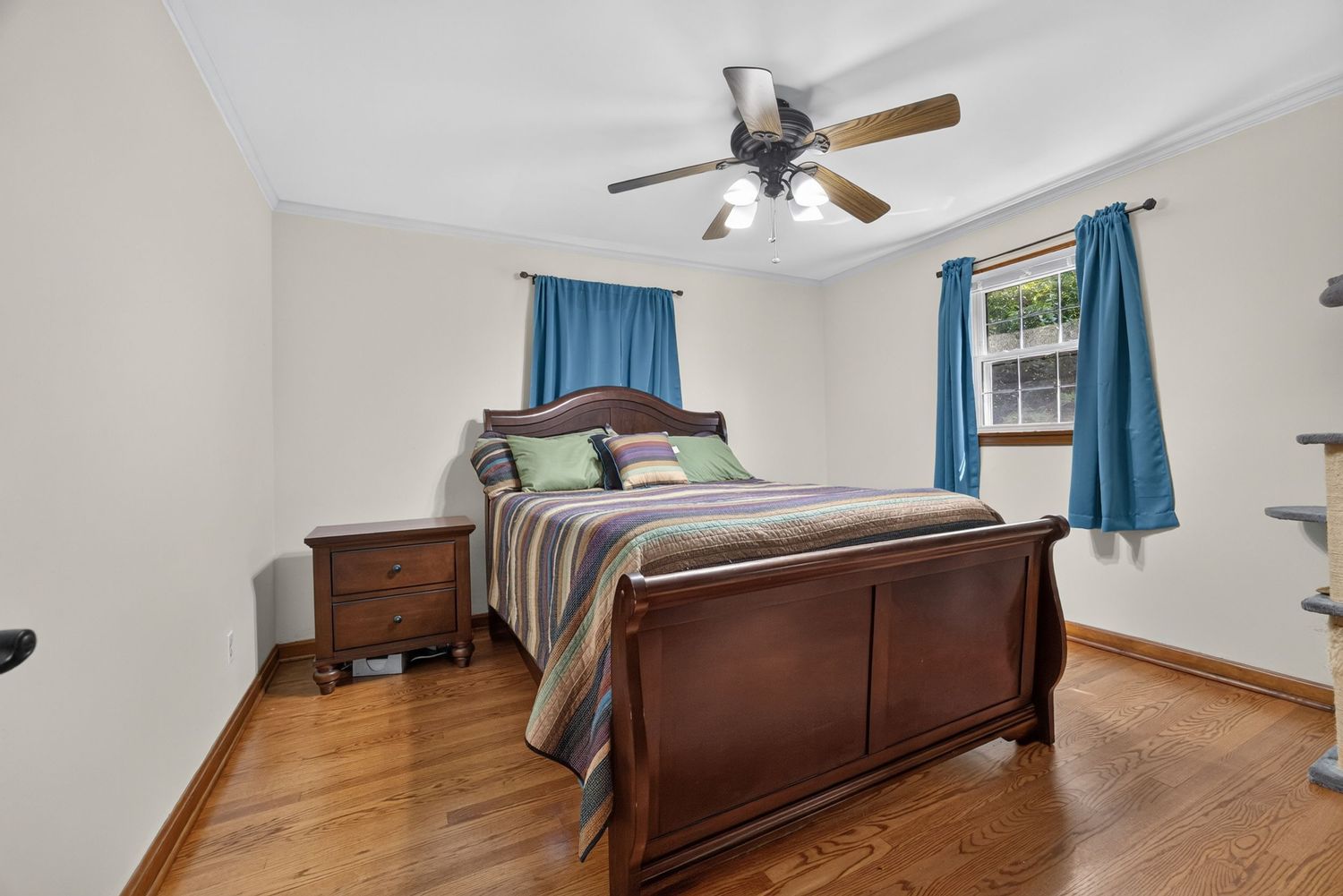 Cozy bedroom with dark wood sleigh bed, hardwood floors, blue curtains, and ceiling fan with light fixture.