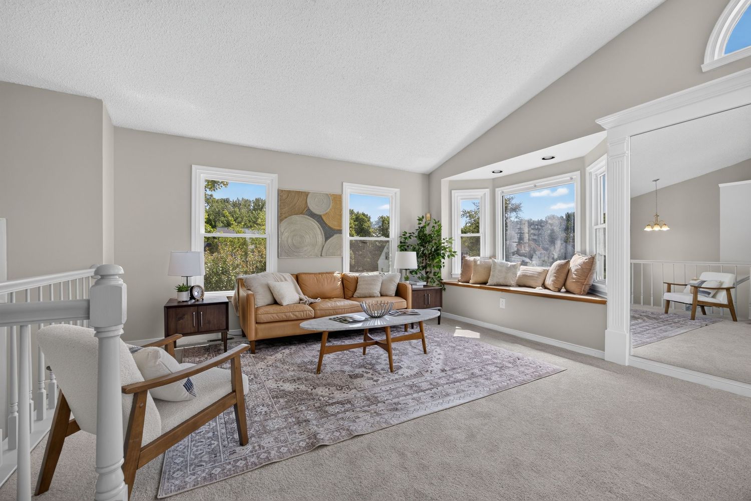 Bright living room with vaulted ceilings, large windows, tan sofa, wood coffee table, and cozy window seat with city views.