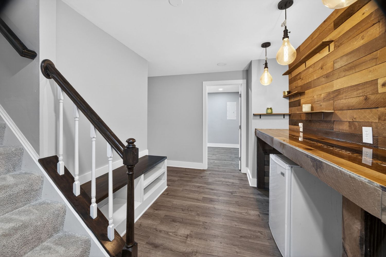 Modern hallway with wood accent wall, pendant lights, staircase, and dark hardwood floors in a stylish home interior.