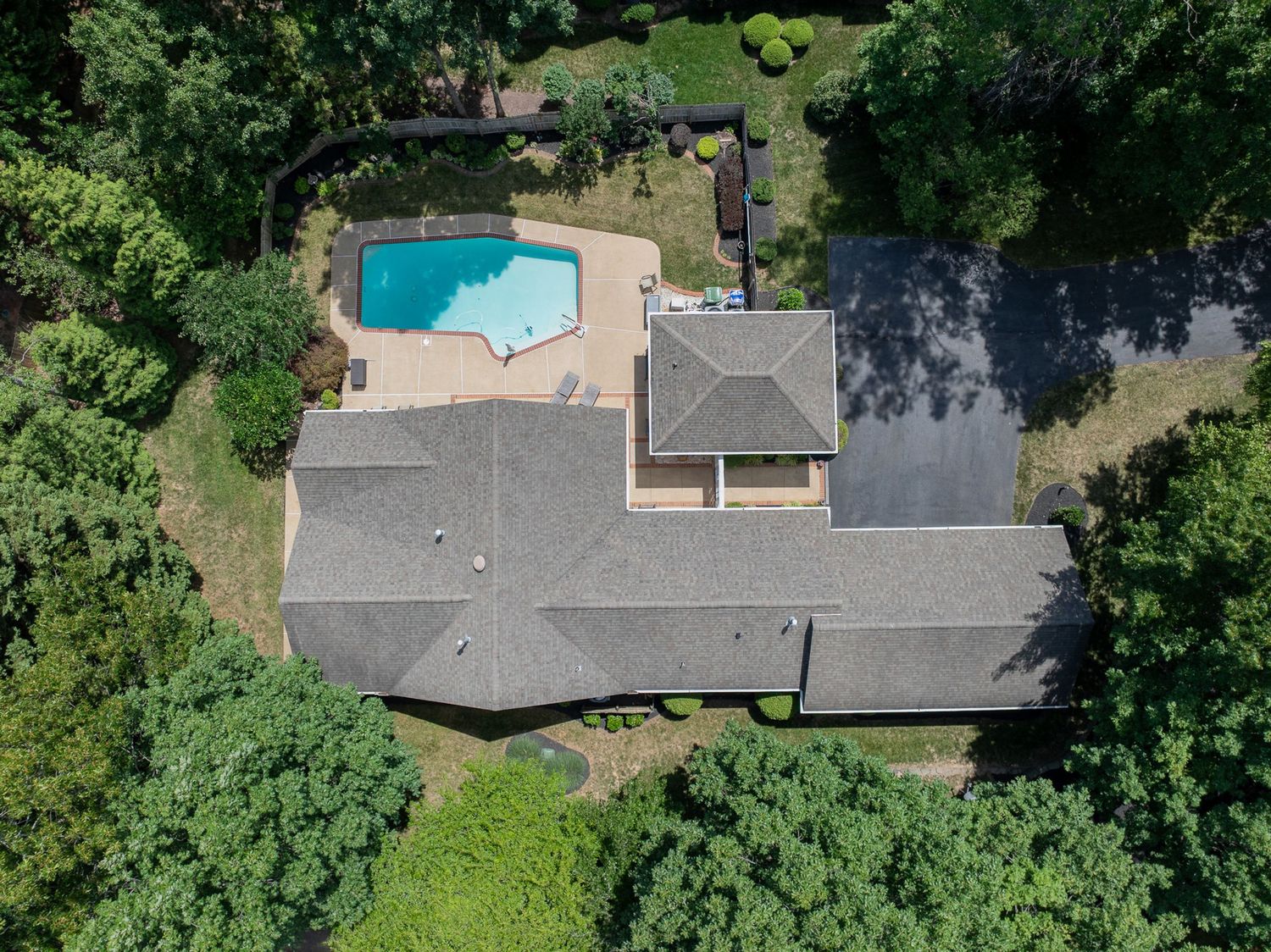 Aerial view of a suburban home with gray roof, backyard pool, and surrounding lush green trees.
