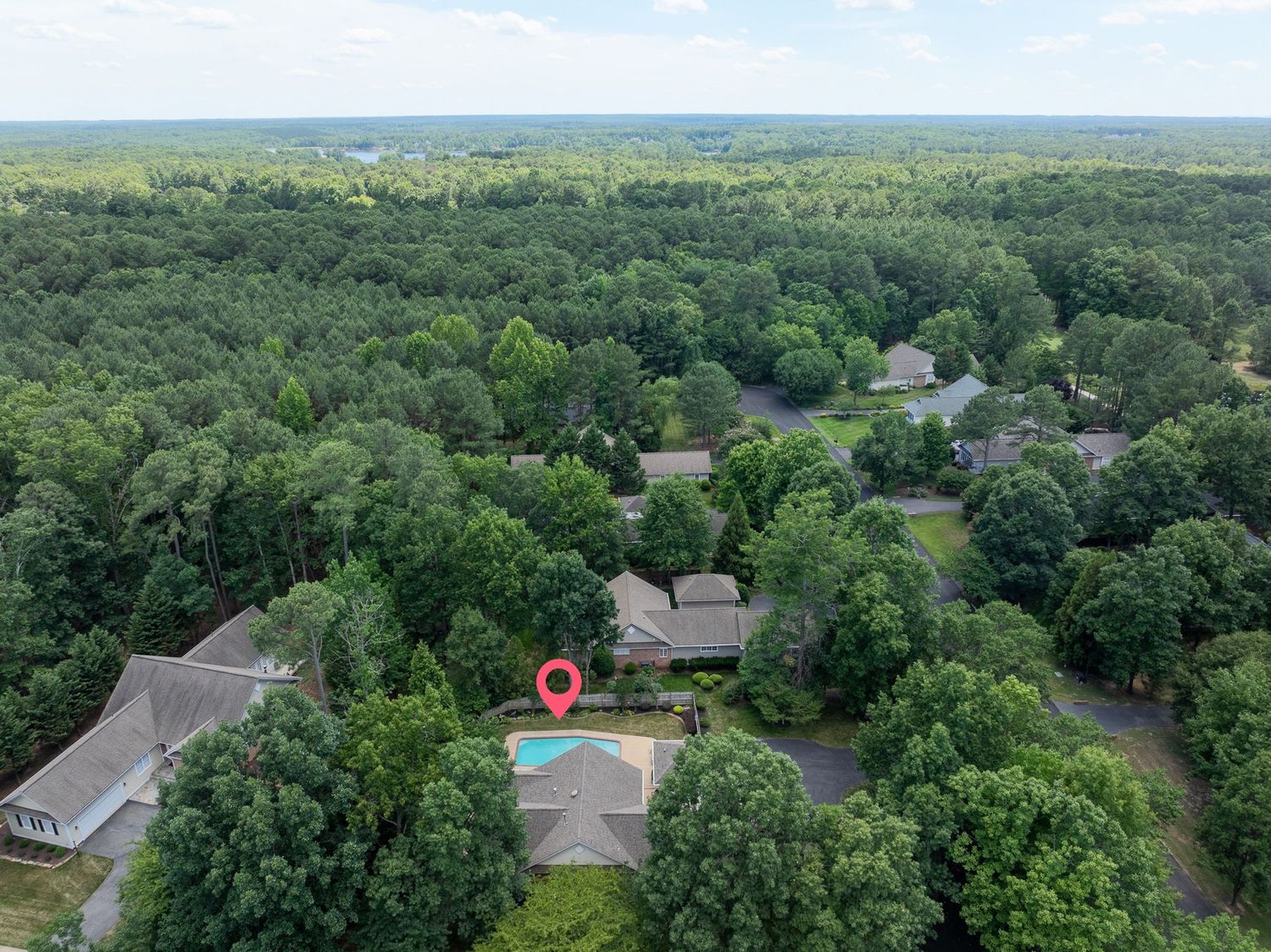 Aerial drone view of a suburban home with a swimming pool surrounded by lush green trees and neighboring houses.