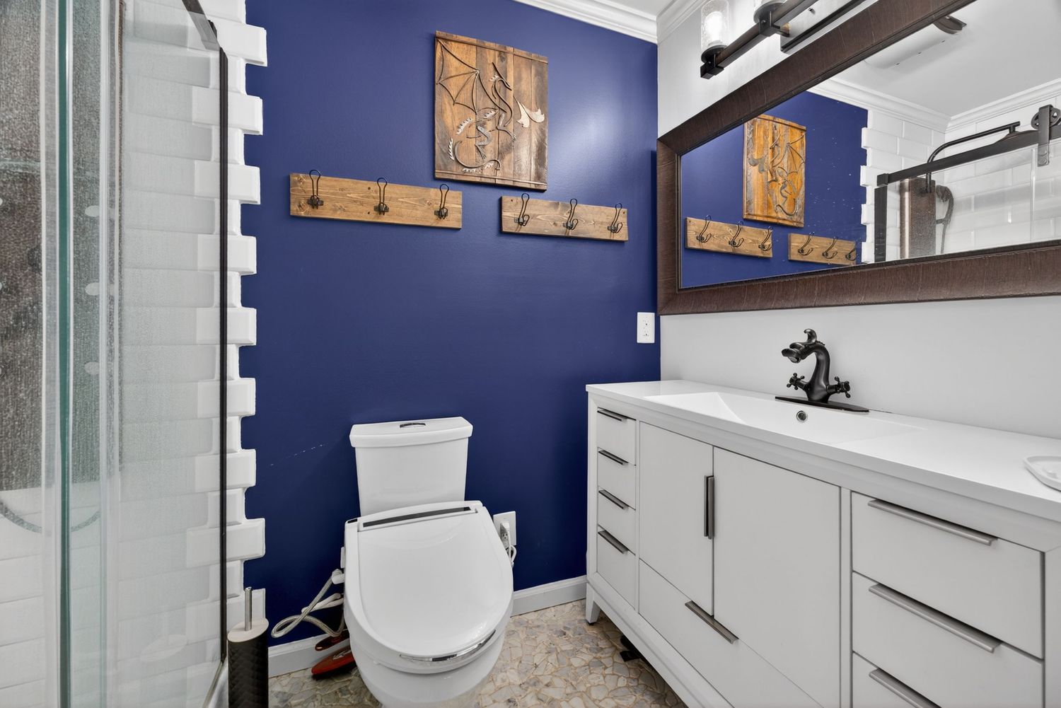 Modern bathroom with bold blue accent wall, white toilet, white vanity with mirror, and tiled walk-in shower.