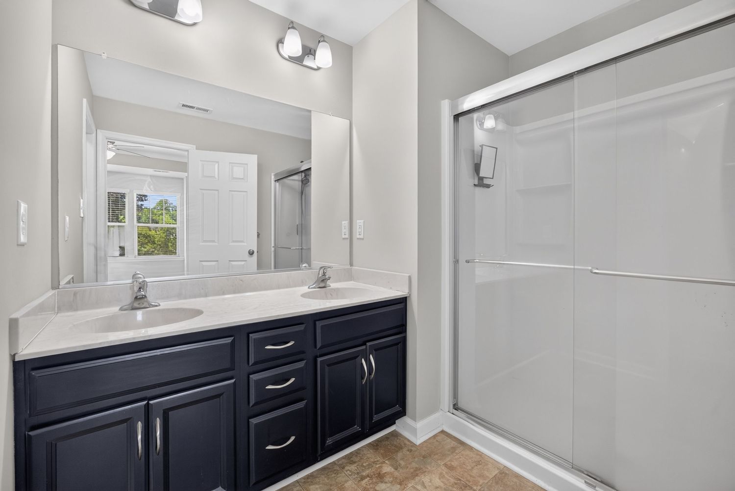 Modern bathroom with dark navy double vanity, white countertop, large mirror, and glass-enclosed walk-in shower.