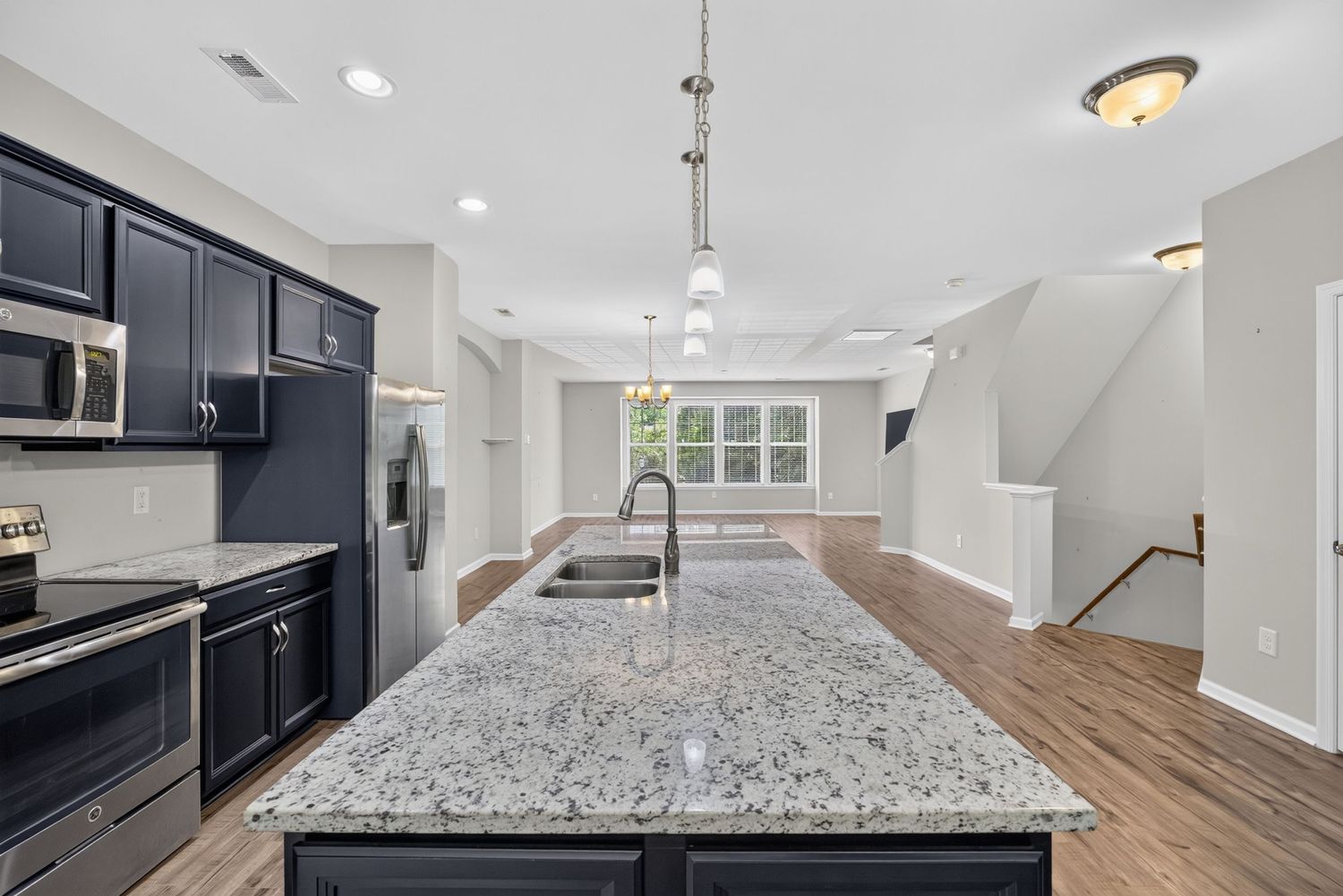 Modern kitchen with granite island, navy cabinets, stainless appliances, pendant lights, and hardwood floors.