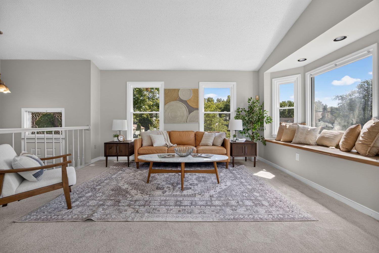 Bright living room with vaulted ceilings, large windows, leather sofa, wood coffee table, and built-in window seat with cushions.