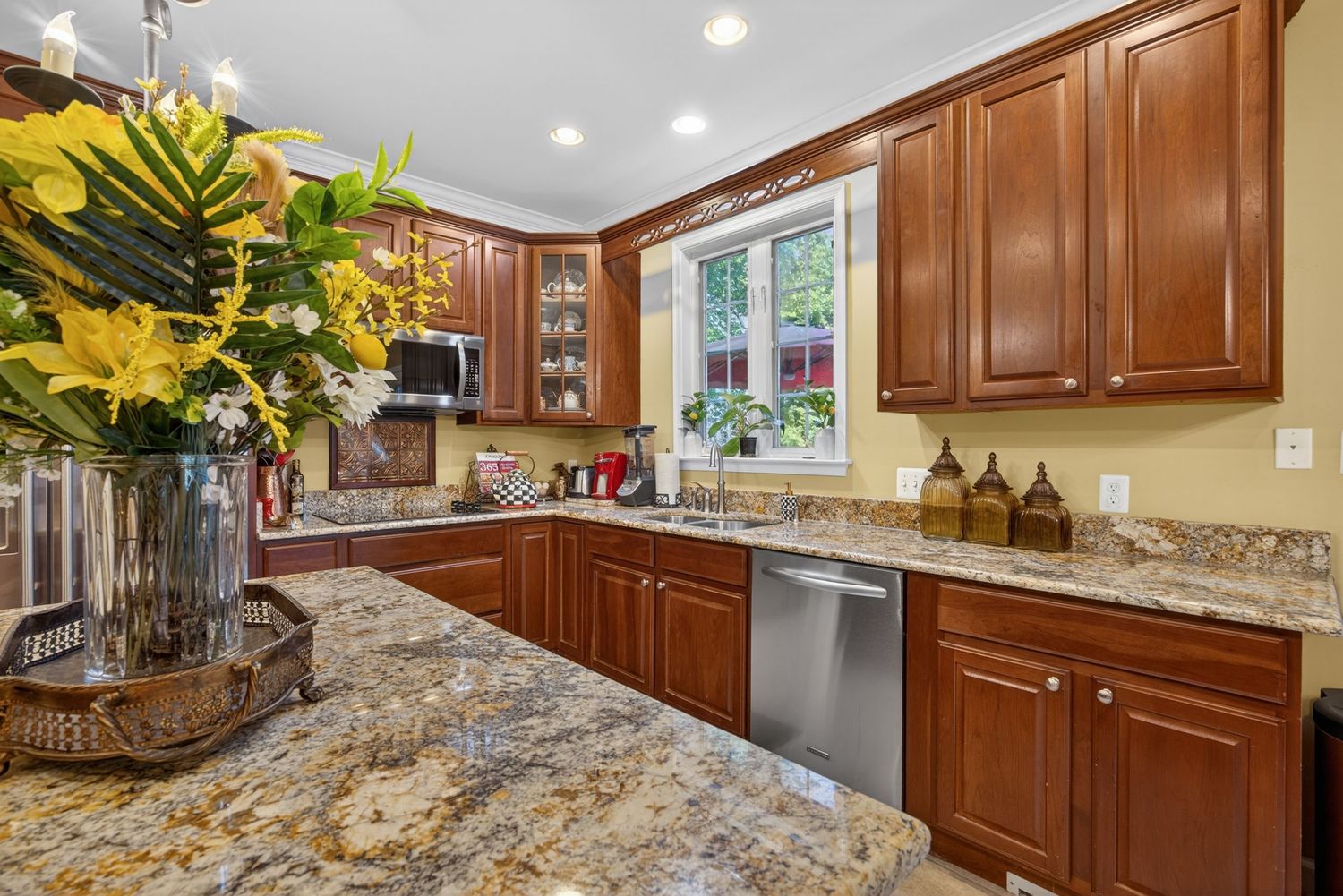 Elegant kitchen with cherry wood cabinets, granite countertops, stainless steel dishwasher, and tropical floral arrangement.