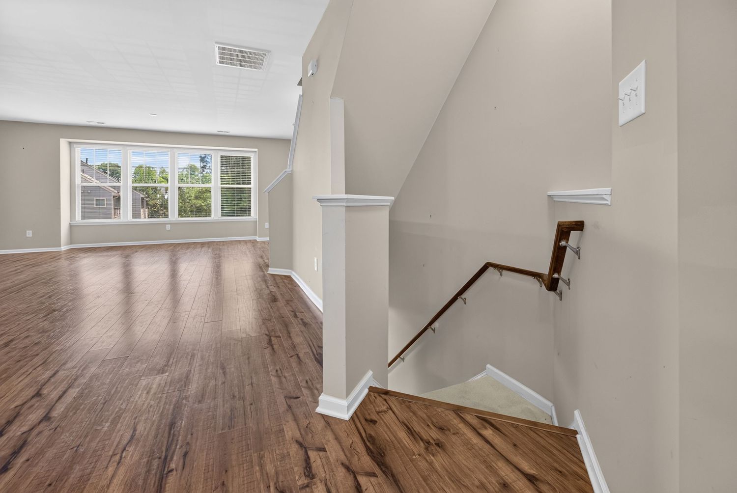 Bright open living area with dark hardwood floors, white trim, and staircase with wood railing leading to upper level.