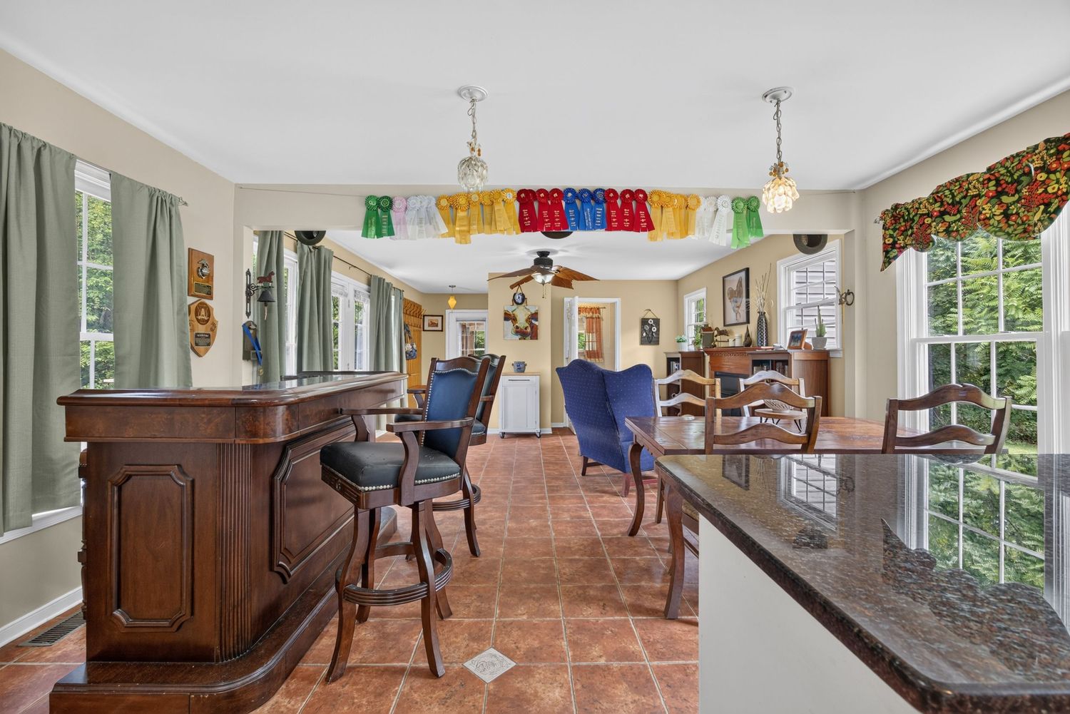 Bright open-concept kitchen and living area with dark wood bar, granite counters, tile floors, and colorful party decorations.