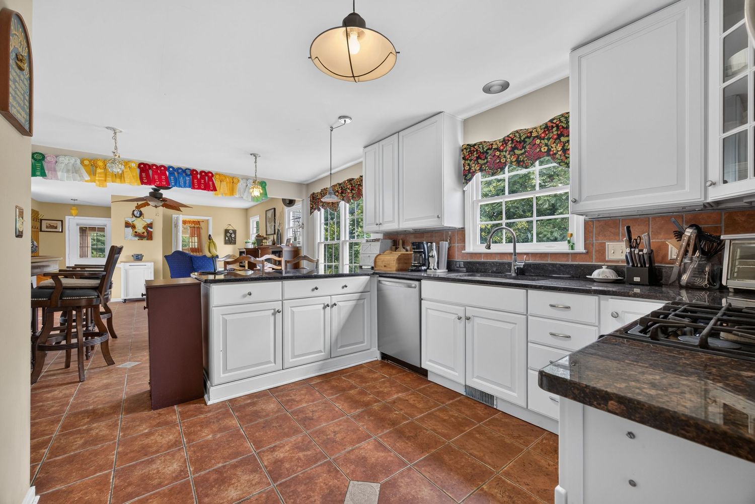 Bright kitchen with white cabinets, dark granite counters, terracotta tile floors, and a center island with pendant lighting.