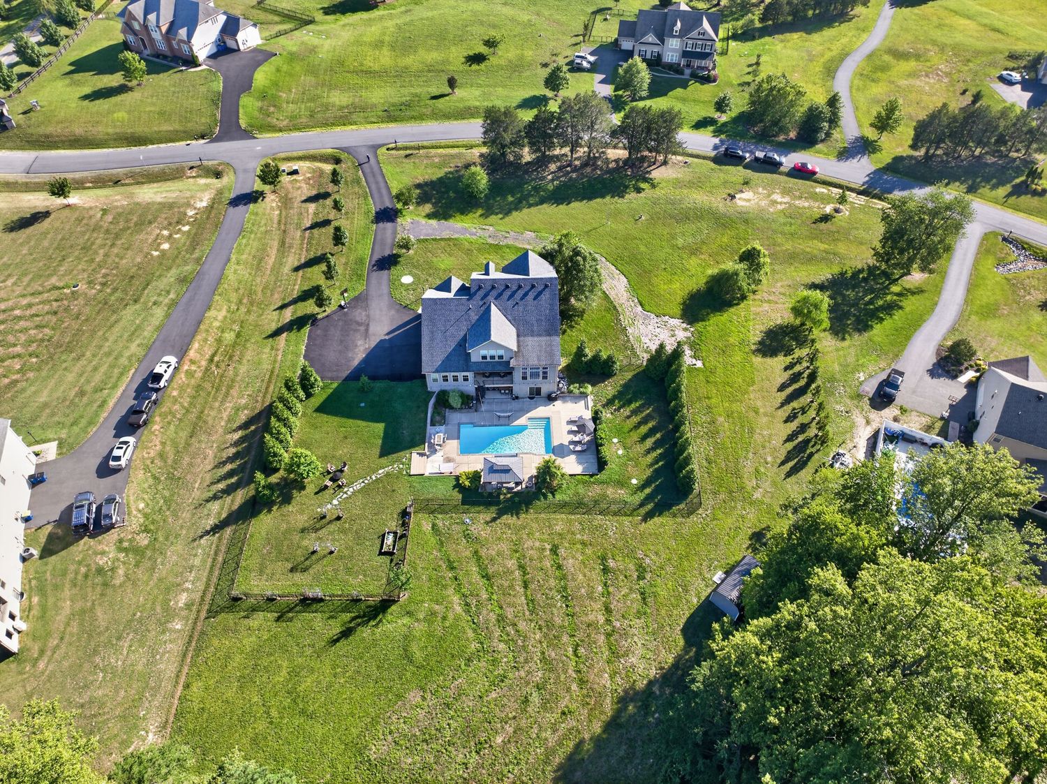 Aerial view of a large suburban home with a swimming pool surrounded by lush green lawns and winding roads.