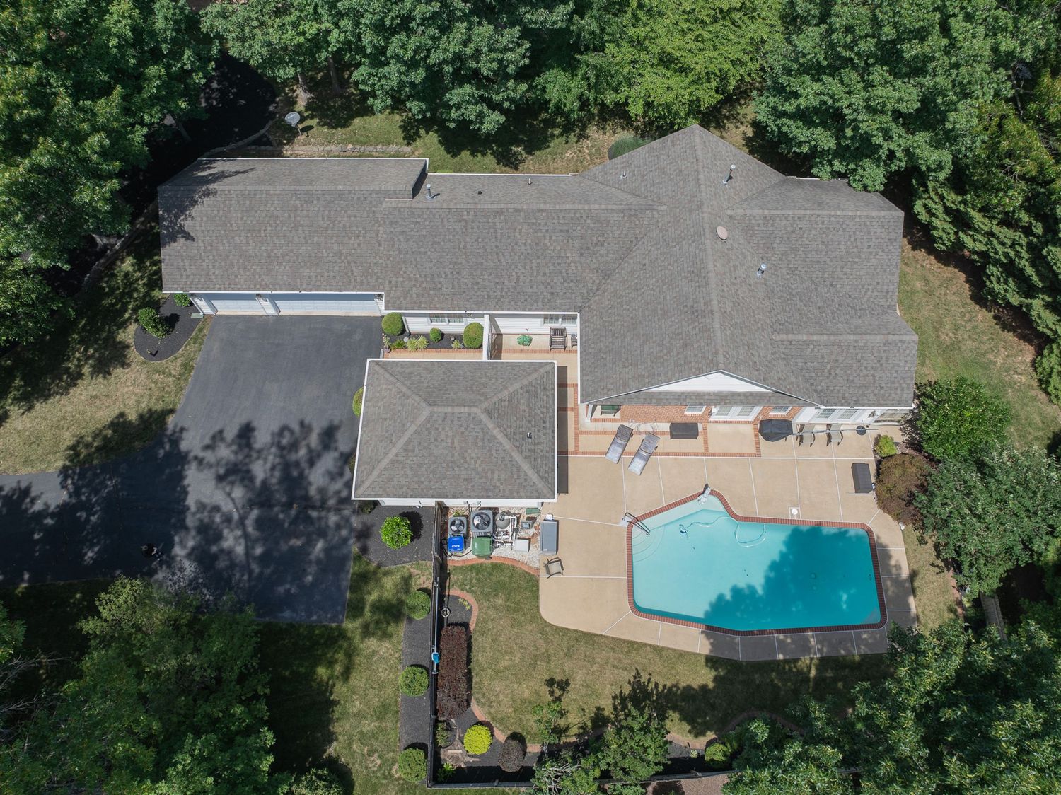Aerial view of a large home with a gray roof, outdoor pool, patio, and lush green trees surrounding the property.