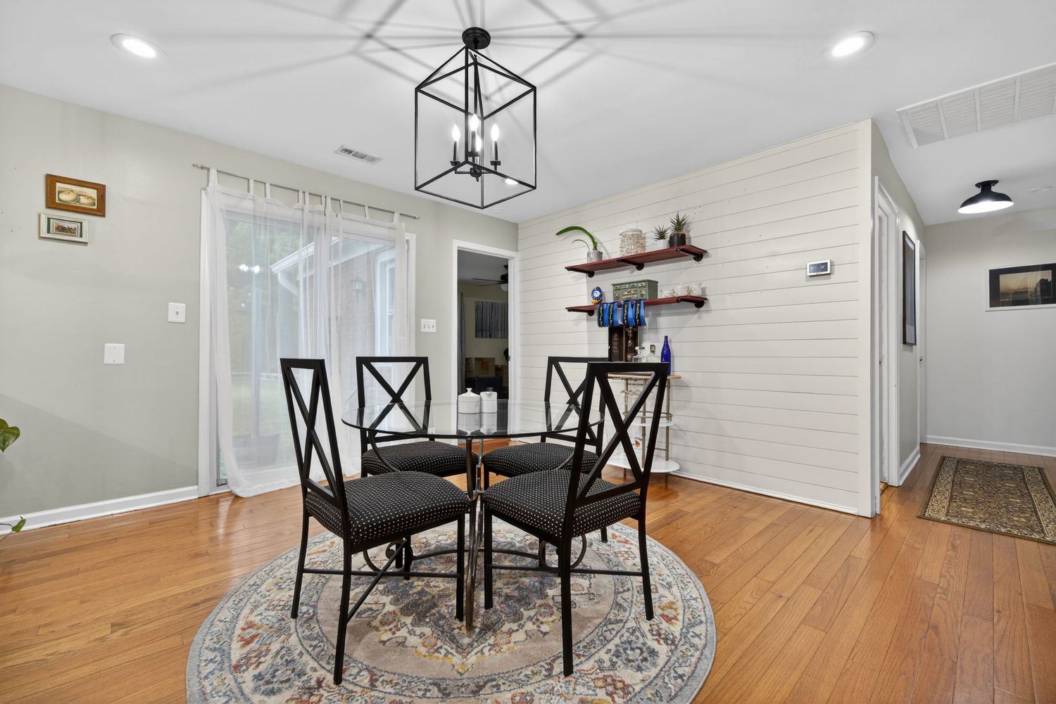 Bright dining area with black metal table, four chairs, round rug, hardwood floors, and modern chandelier.