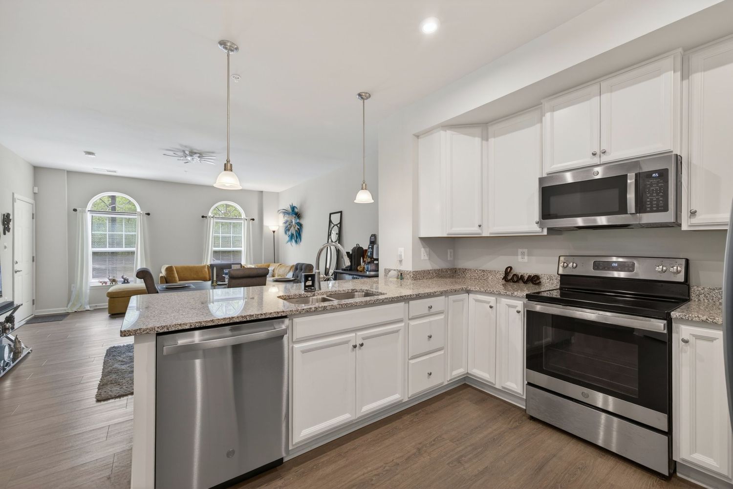 Modern kitchen with white cabinets, stainless steel appliances, granite countertops, and open floor plan with hardwood floors.