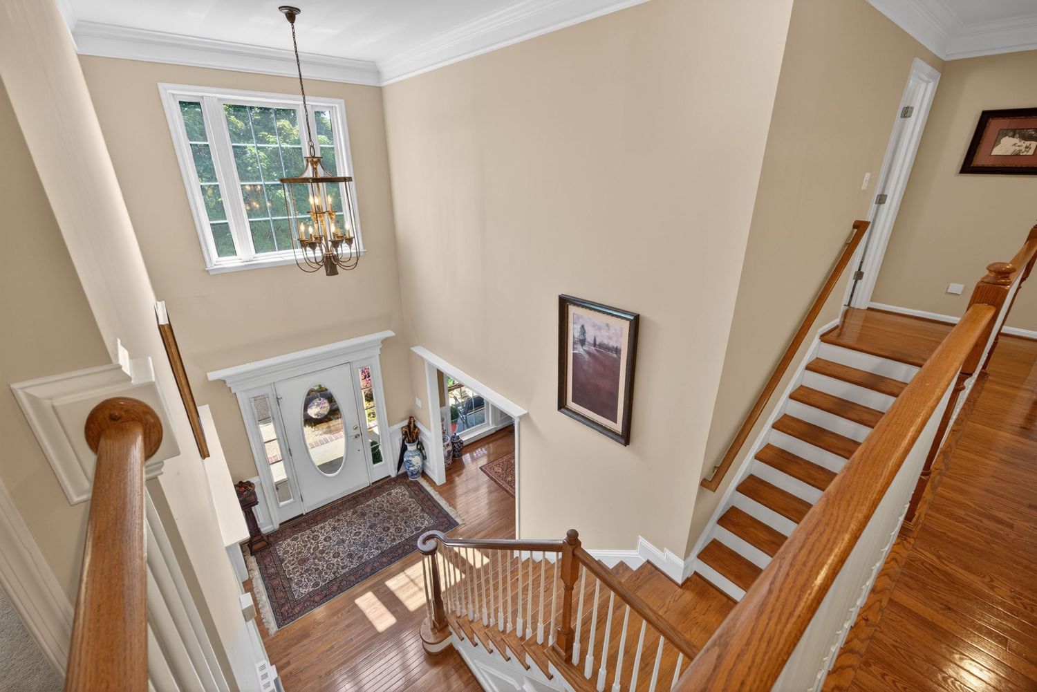 Elegant two-story foyer with hardwood floors, wooden staircase, chandelier, and natural light from a transom window.