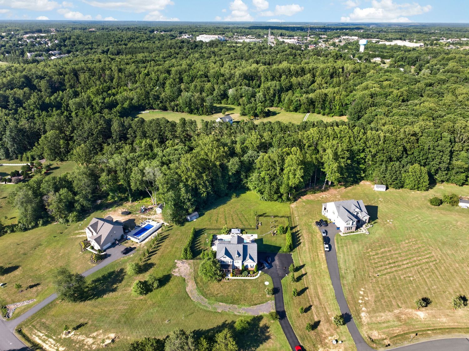 Aerial view of luxury homes surrounded by lush green trees and manicured lawns in a spacious suburban neighborhood.