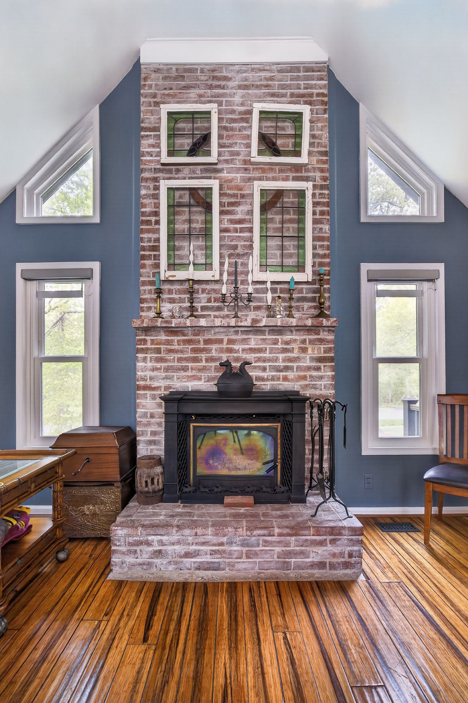 Rustic brick fireplace with wood stove insert in a vaulted ceiling room with blue walls and hardwood floors.