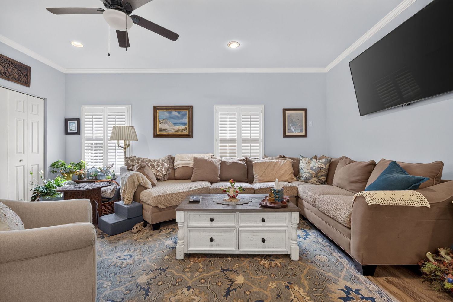 Cozy living room with large L-shaped sectional sofa, white coffee table, ceiling fan, and wall-mounted TV.