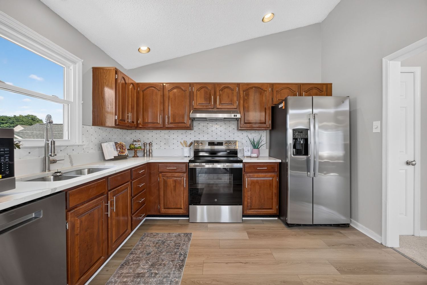 Modern kitchen with brown cabinets, stainless steel appliances, subway tile backsplash, and light hardwood floors.
