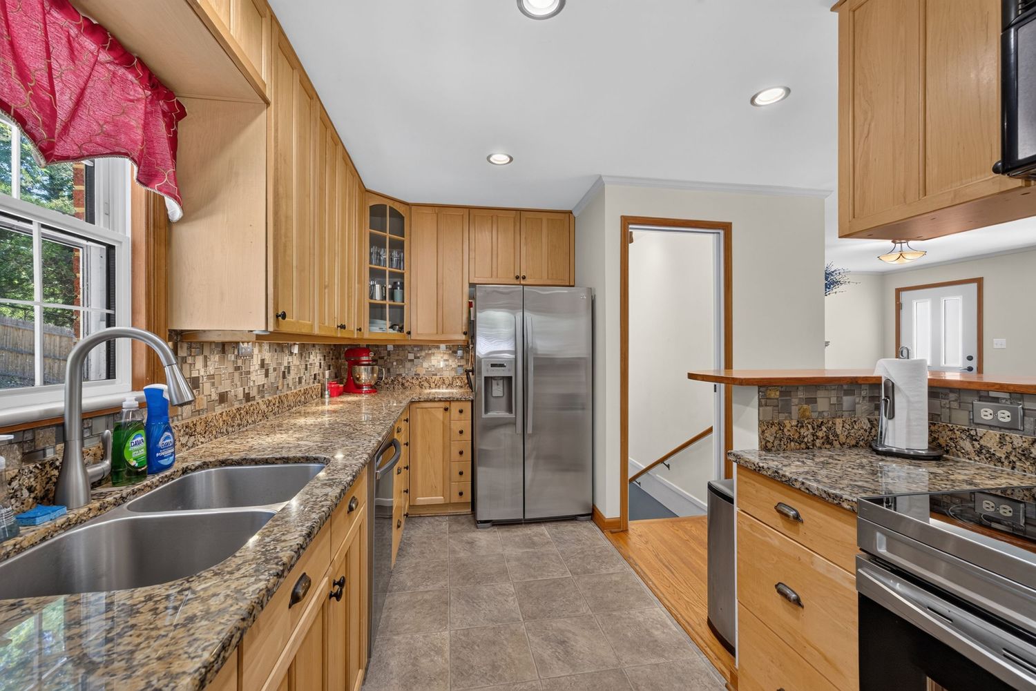 Modern kitchen with maple cabinets, granite countertops, stainless steel appliances, and stone tile backsplash.
