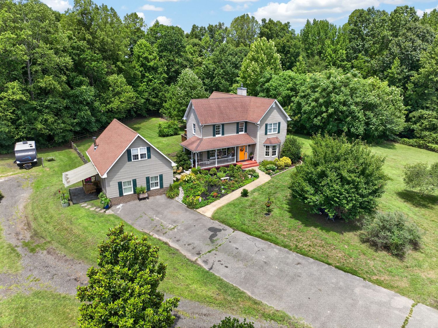 Aerial view of a two-story colonial home with a circular driveway, surrounded by lush green trees and manicured lawn.