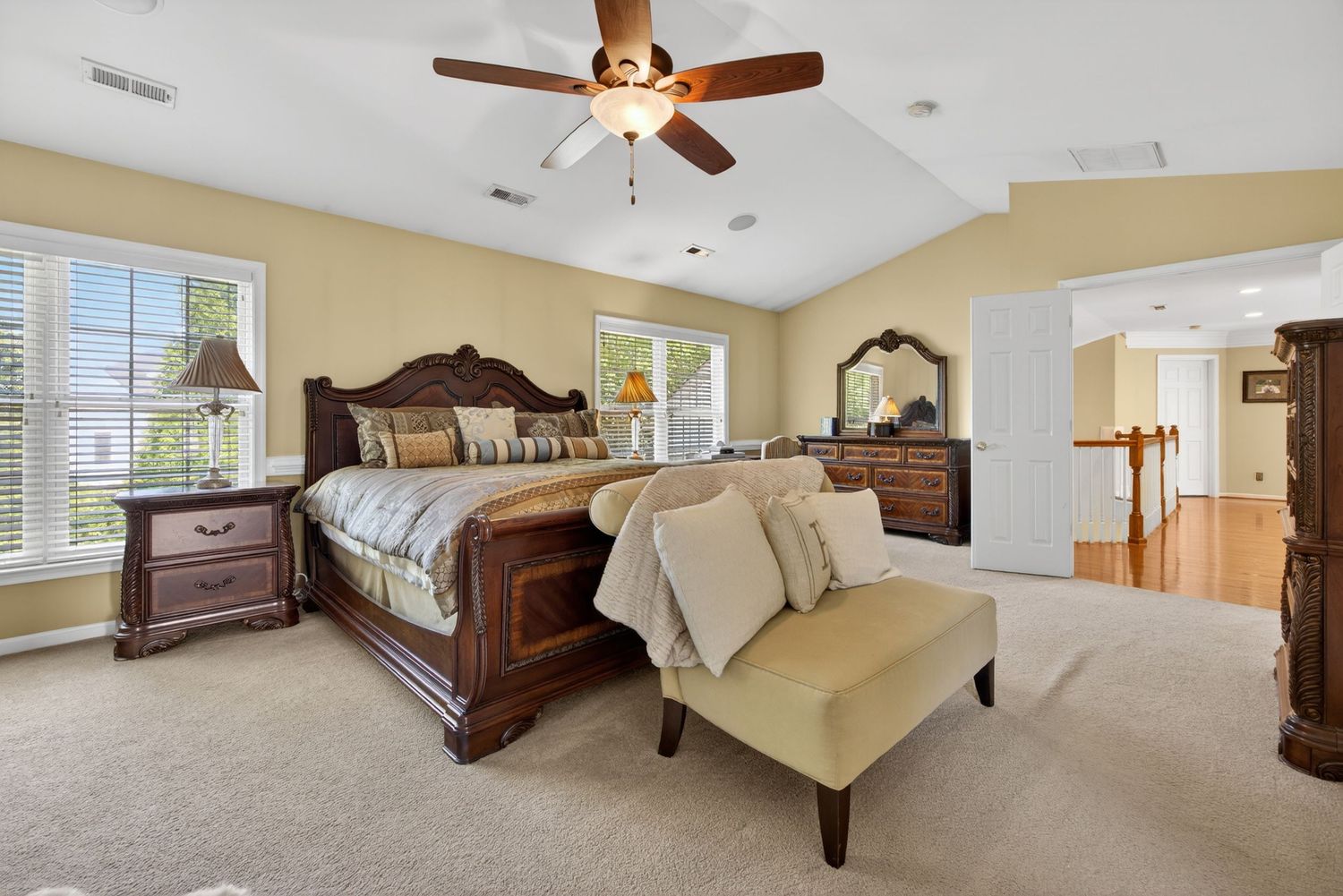 Spacious master bedroom with dark wood furniture, ceiling fan, neutral carpet, and natural light from multiple windows.