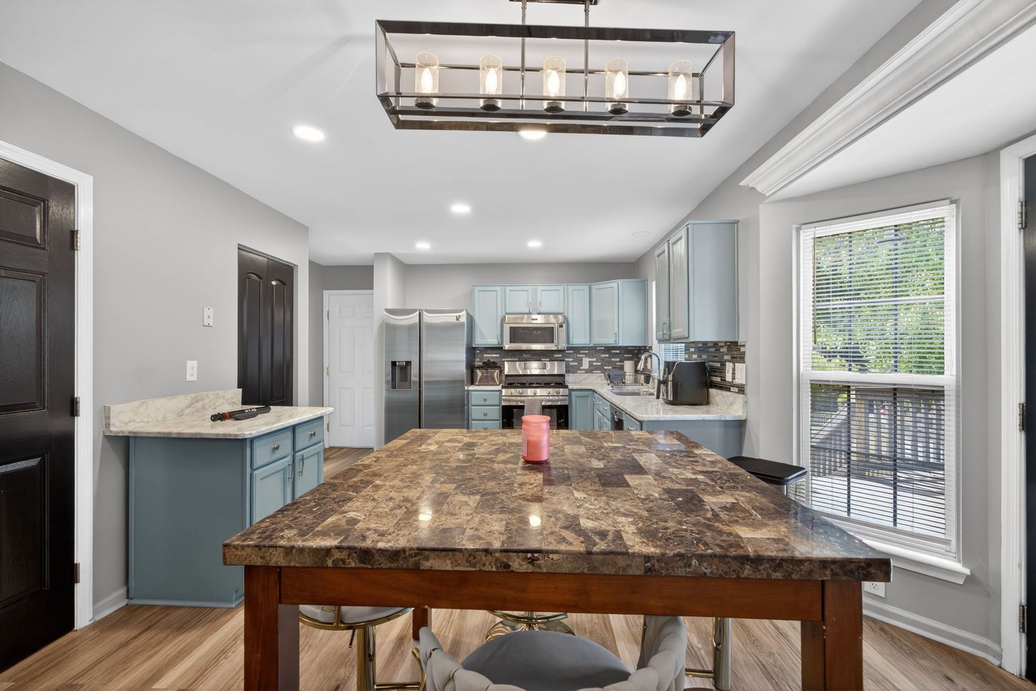 Modern kitchen with blue-gray cabinets, stainless steel appliances, granite island, and hardwood floors bathed in natural light.