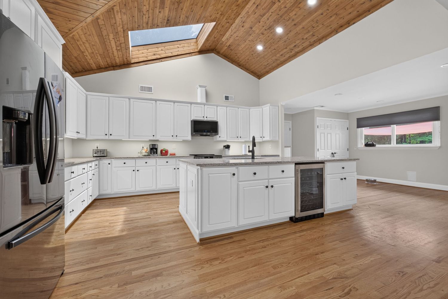 Bright white kitchen with vaulted wood ceiling, skylight, center island, and hardwood floors.