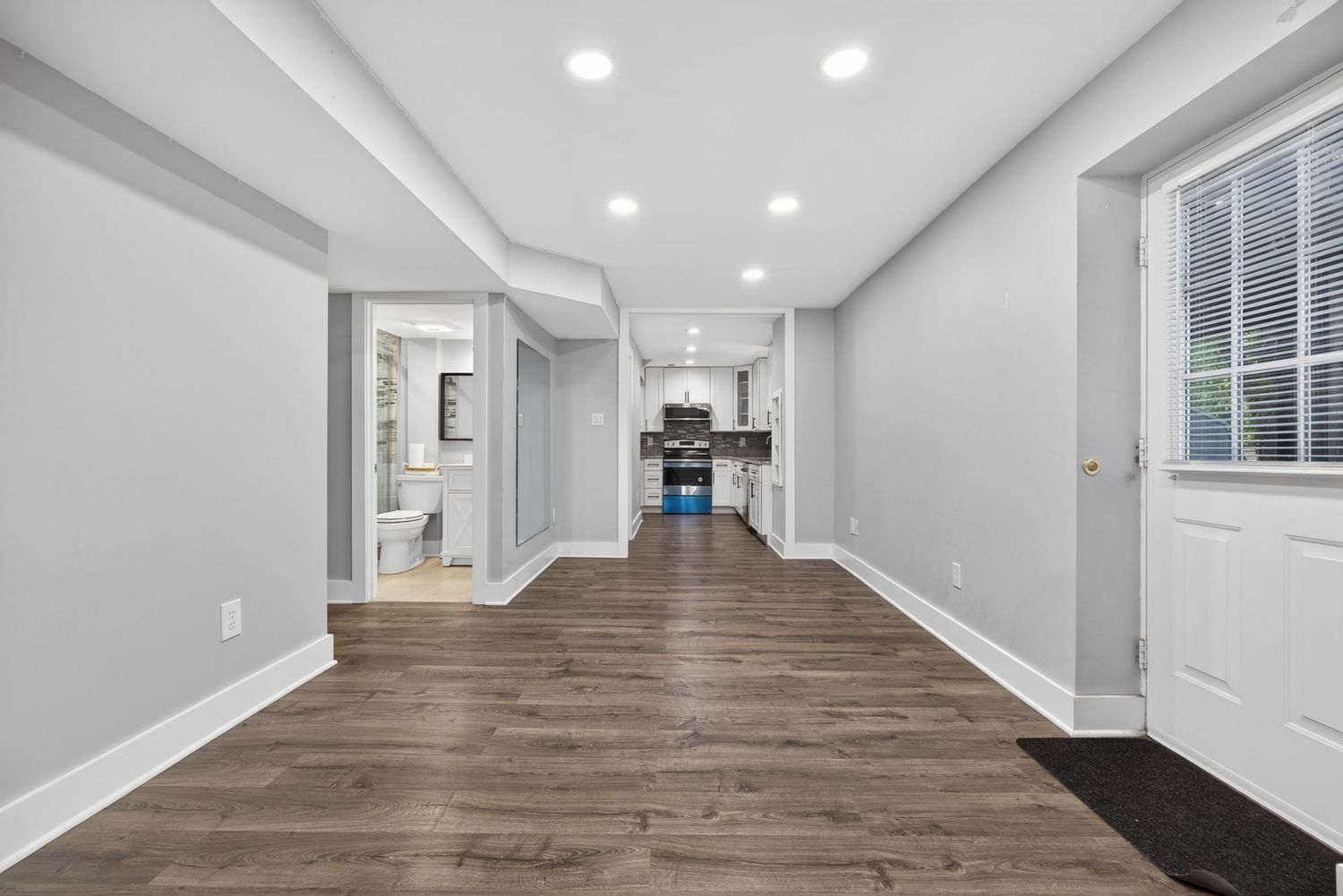 Spacious open-concept living area with dark hardwood floors, recessed lighting, white walls, and a view into the kitchen.