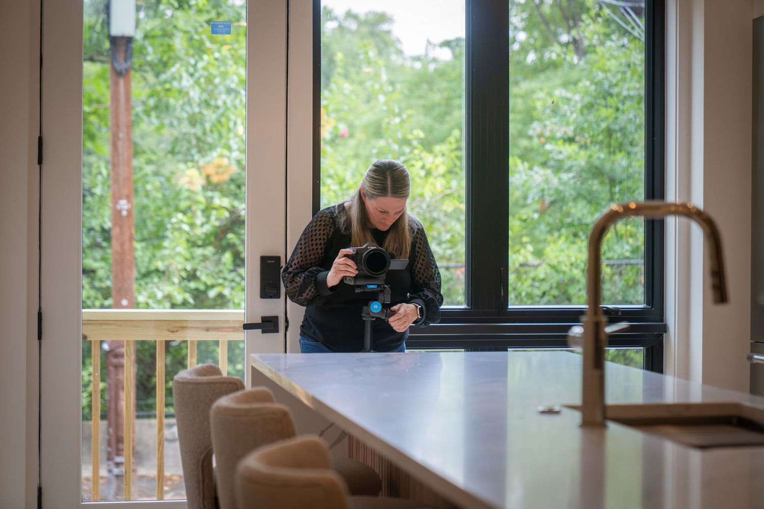 Photographer capturing interior kitchen details with large windows and lush greenery in a modern home.