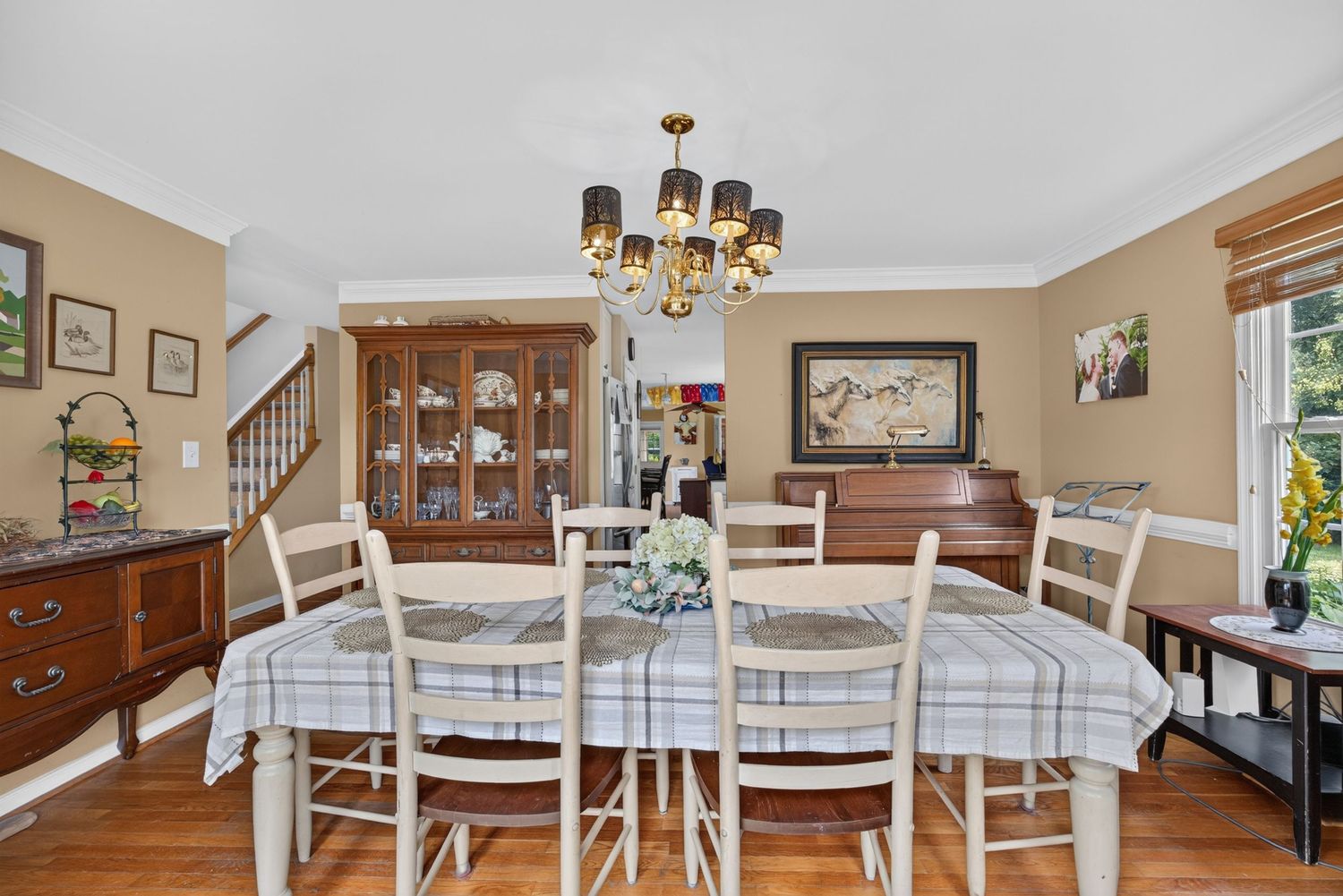 Elegant dining room with plaid tablecloth, white chairs, wood floors, china cabinet, and brass chandelier.