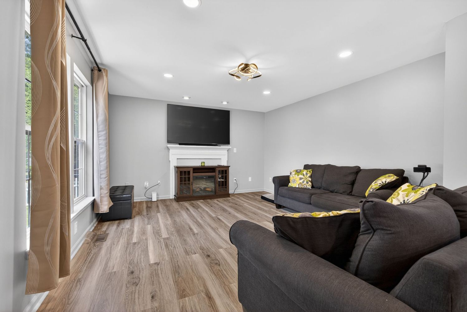 Bright living room with gray sectional sofa, electric fireplace, wall-mounted TV, and light hardwood floors.