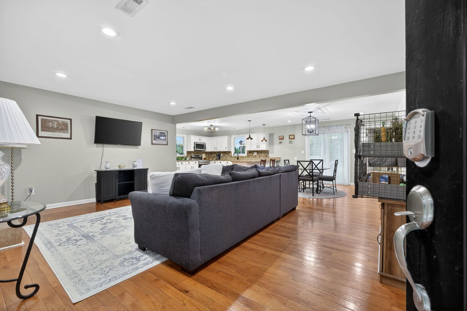 Spacious open-concept living room with hardwood floors, gray sectional sofa, fireplace, and modern kitchen in background.