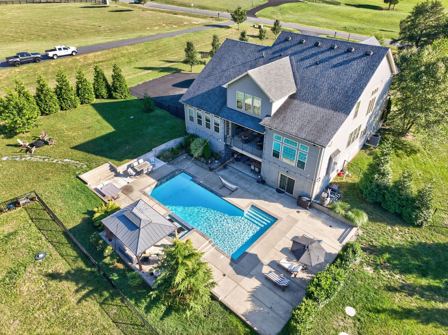 Aerial view of a large suburban home with a rectangular pool, patio, and expansive green lawn.
