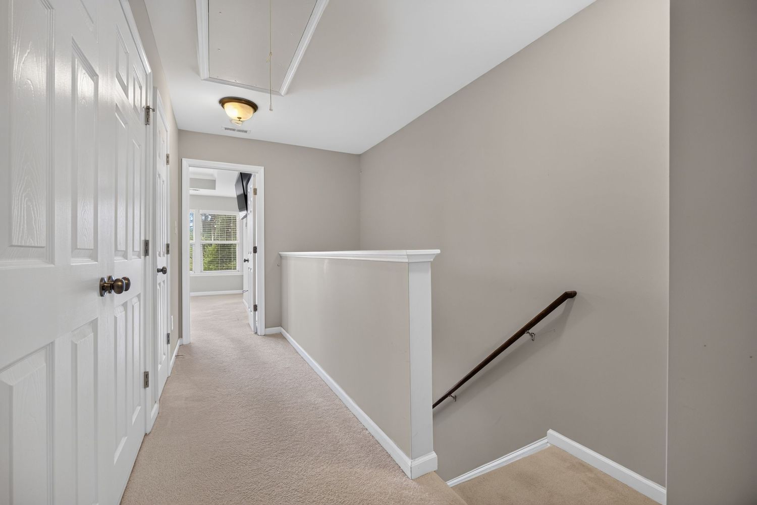 Bright upstairs hallway with gray walls, white trim, carpet flooring, and staircase railing leading to a windowed room.