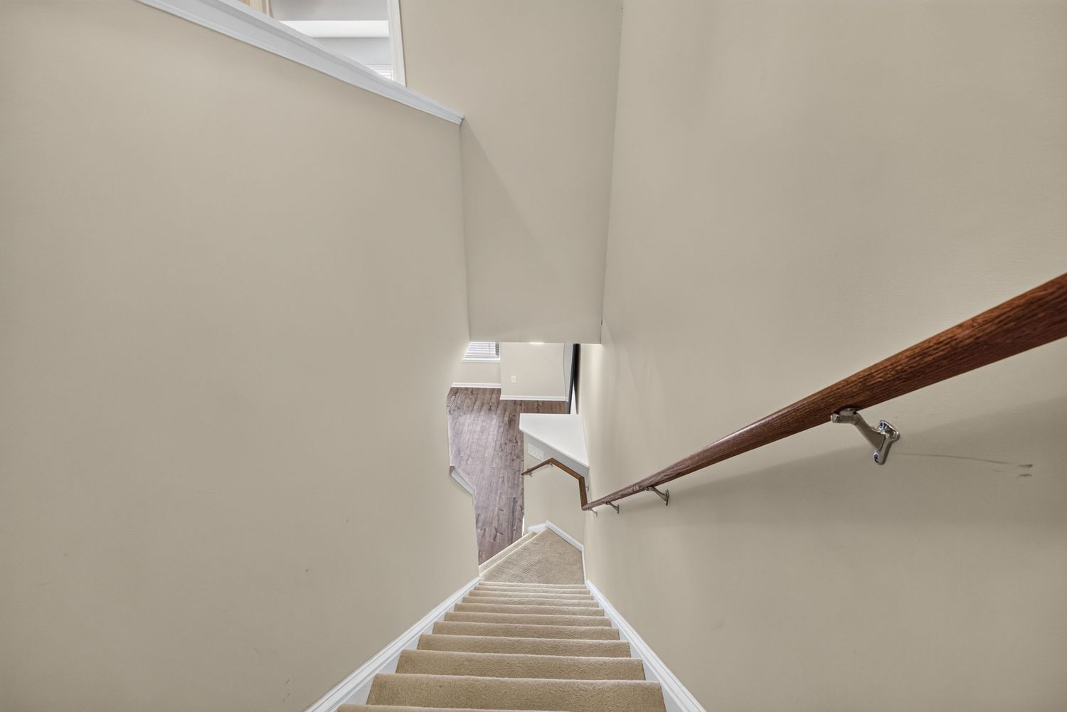 White staircase with wooden handrail and metal brackets leading downward in a bright, modern home interior.