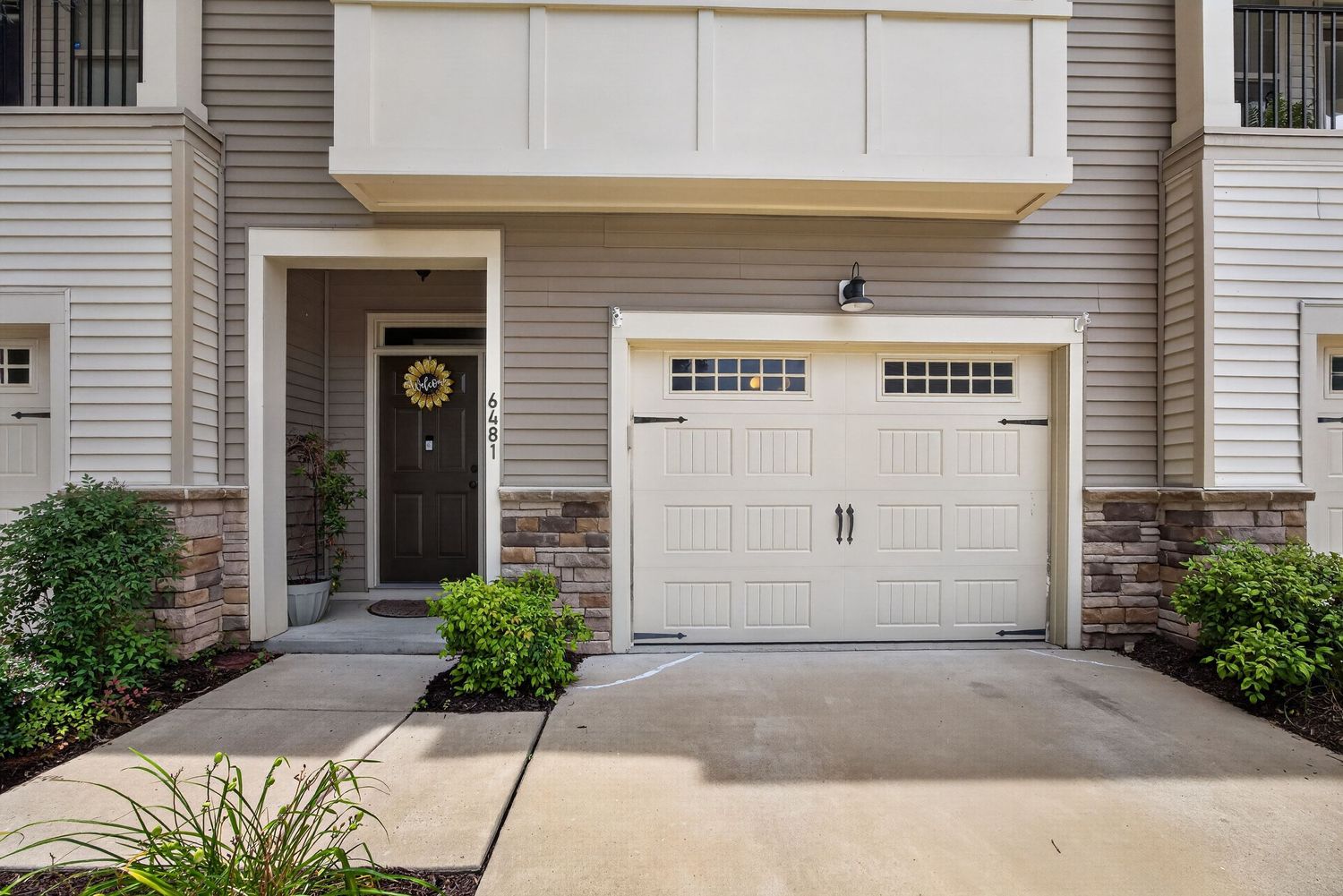 Townhome exterior featuring white garage door, brick accents, dark front door with wreath, and manicured landscaping.