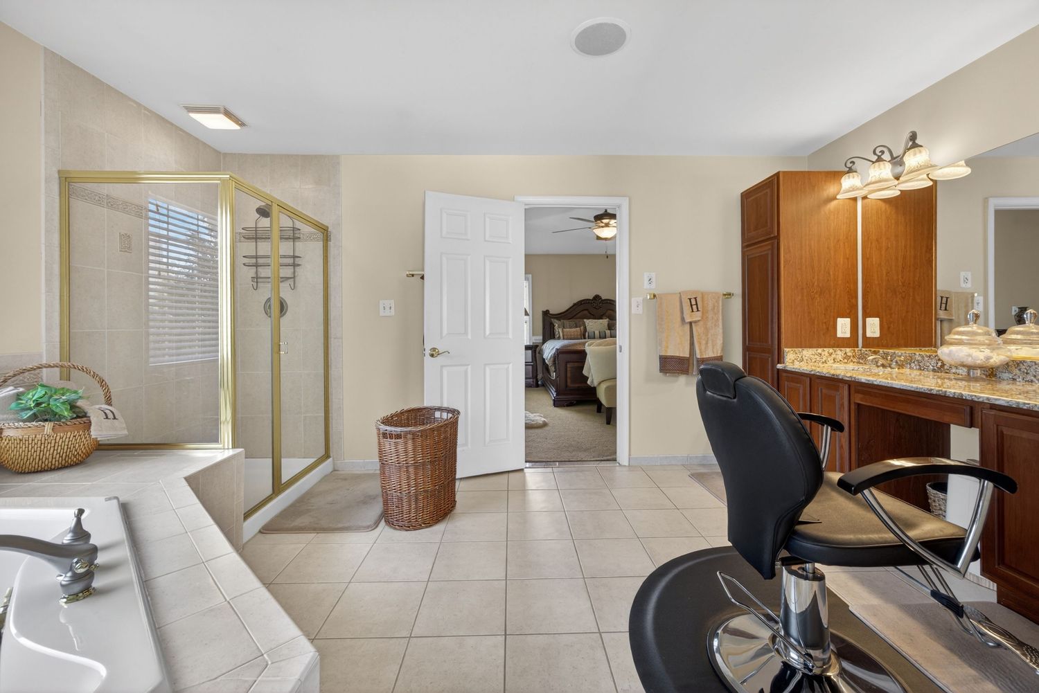 Spacious master bathroom with glass shower, soaking tub, dual vanity, tile floors, and a barber-style chair near the sink.