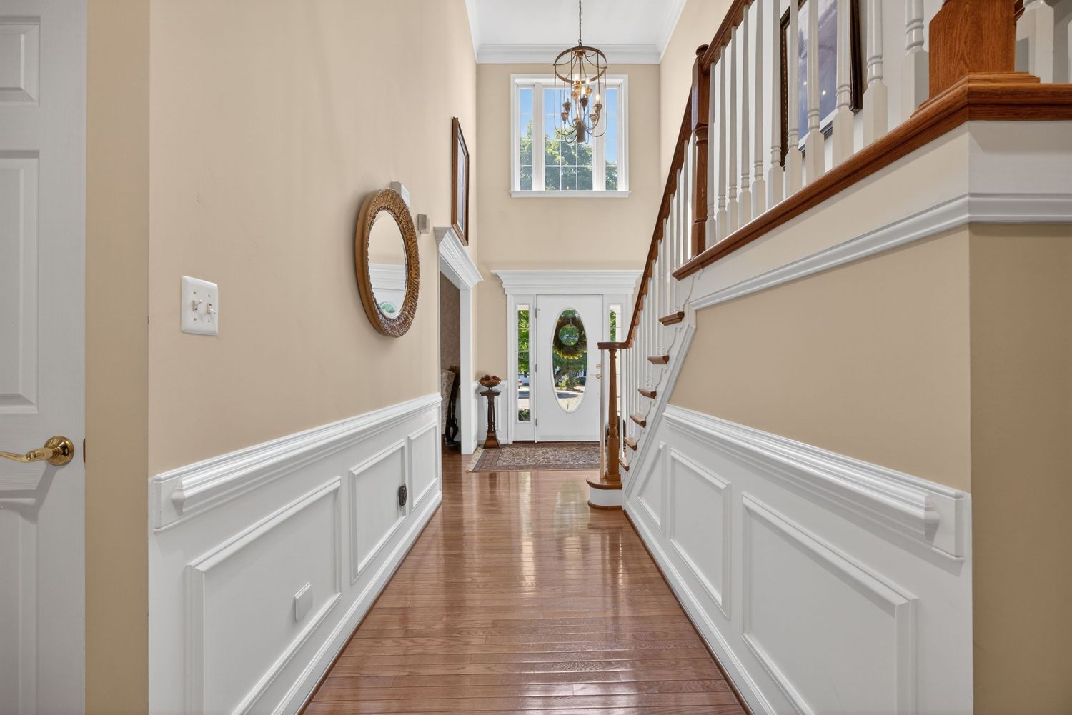 Elegant home entryway with wainscoting, hardwood floors, chandelier, staircase, and a view to the front door.